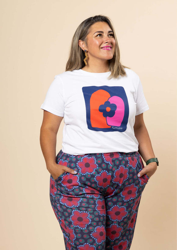 The 2023 Sandra Tee has intersecting orange and pink arches with a flower on a royal blue background